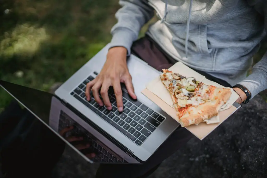 Man working on laptop and eating pizza